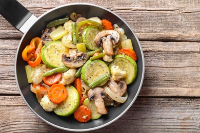 Photo of Different vegetables and mushrooms in frying pan on wooden table, top view