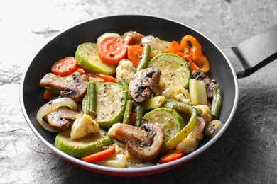 Photo of Different vegetables and mushrooms in frying pan on grey textured table, closeup