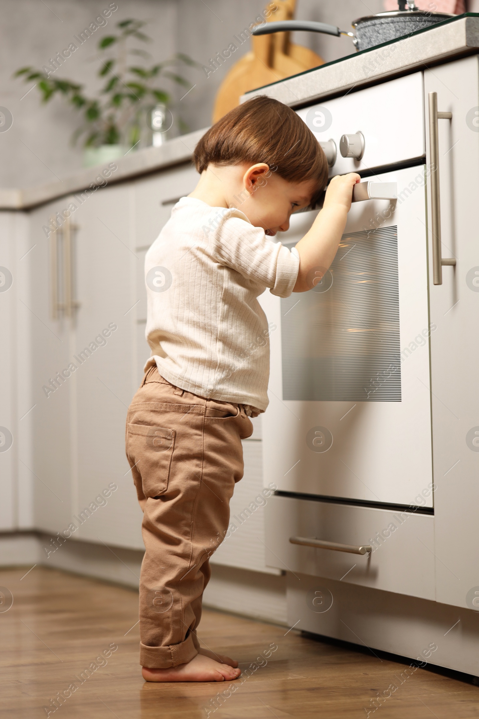 Photo of Little boy playing with oven in kitchen. Dangerous situation