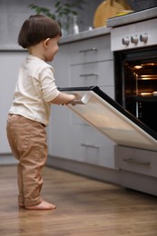 Photo of Little boy playing with oven in kitchen. Dangerous situation