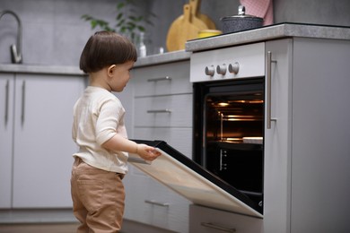 Photo of Little boy playing with oven in kitchen. Dangerous situation