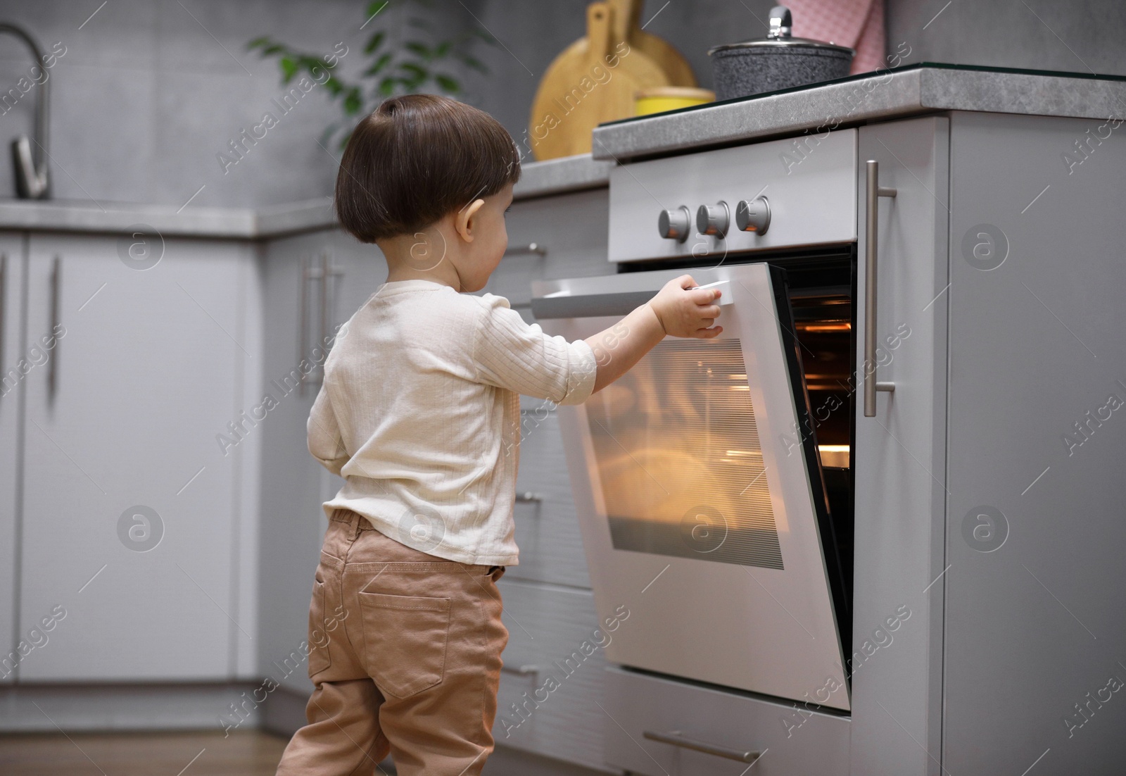 Photo of Little boy playing with oven in kitchen. Dangerous situation