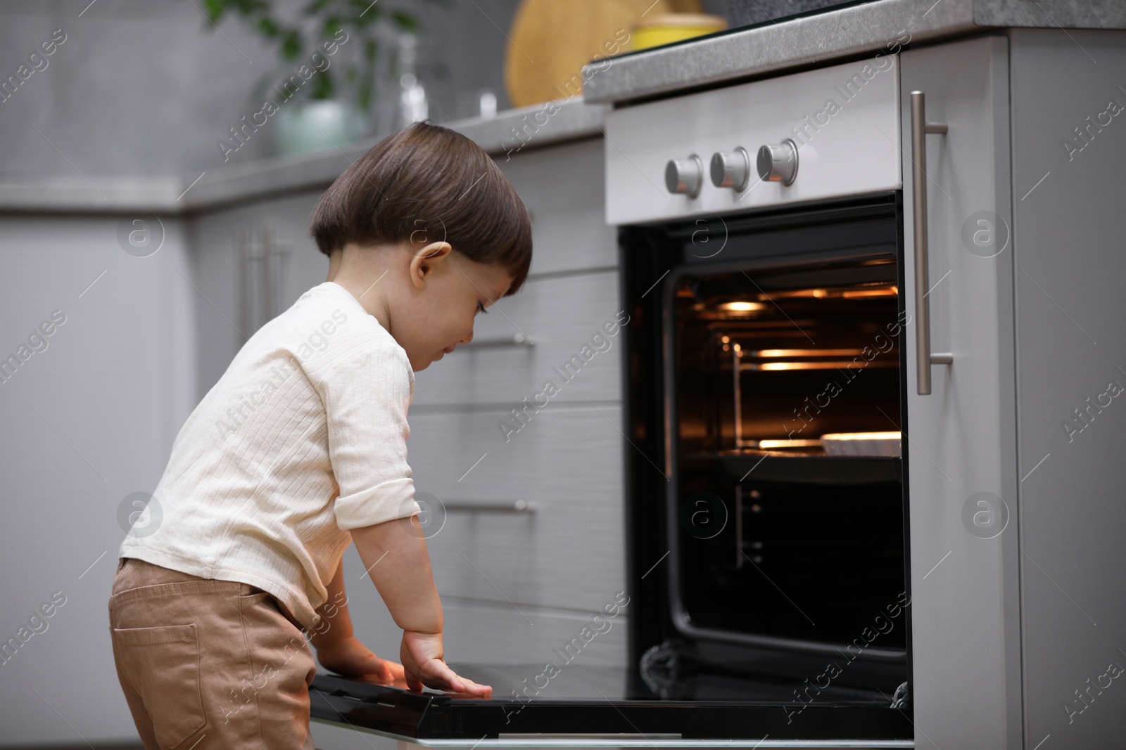 Photo of Little boy playing with oven in kitchen. Dangerous situation