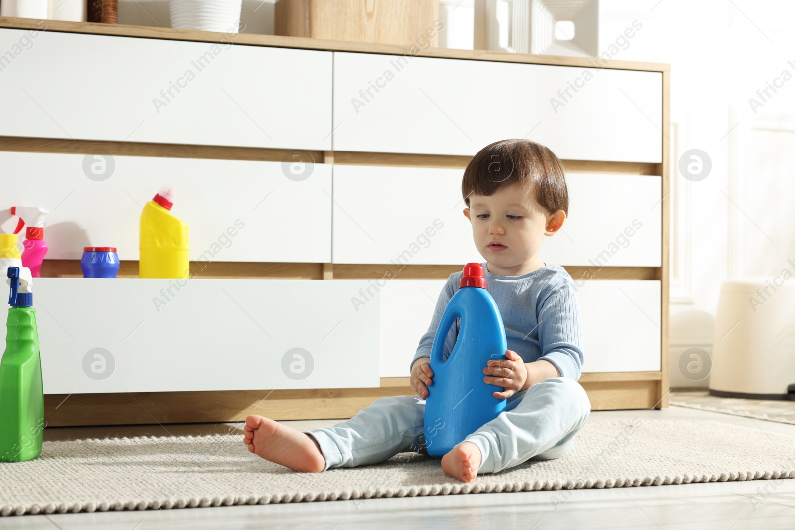 Photo of Little boy playing with bottles of detergents near cabinet at home. Child in danger