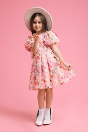 Photo of Stylish little girl wearing oversized high heeled shoes on pink background