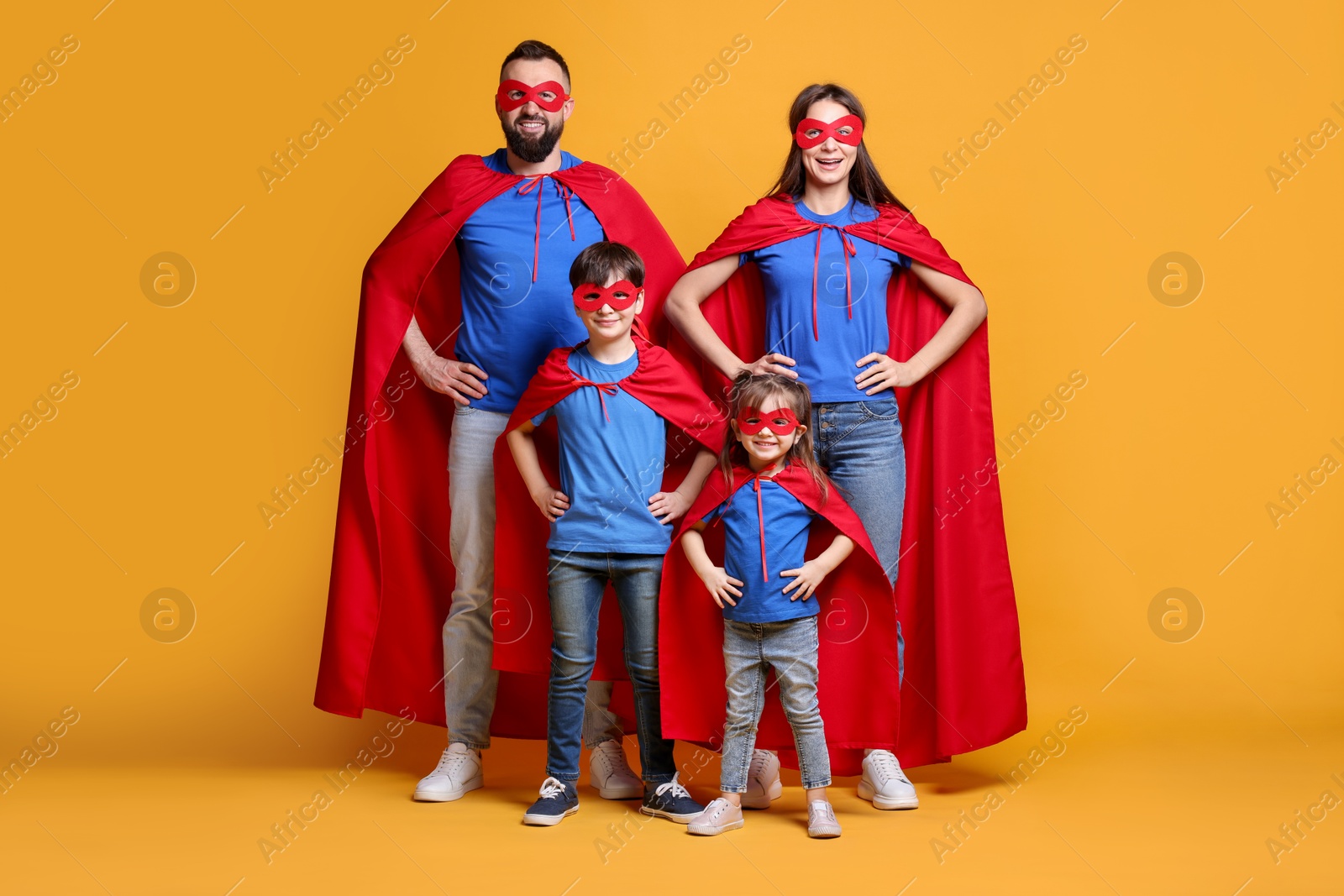 Photo of Parents and their children wearing superhero costumes on orange background