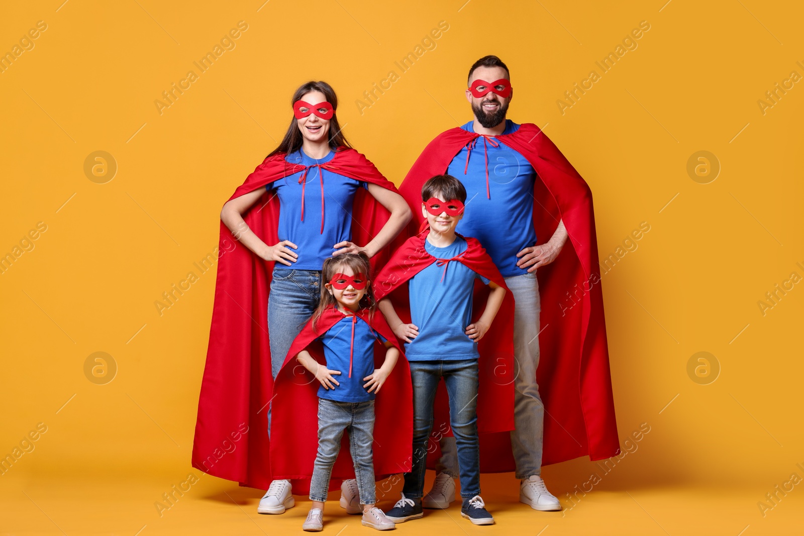 Photo of Parents and their children wearing superhero costumes on orange background