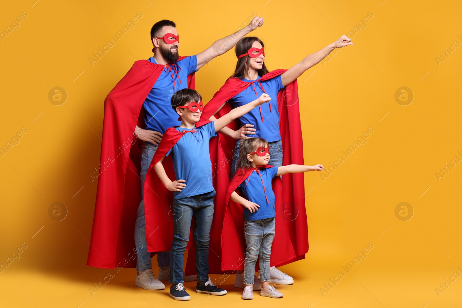 Photo of Parents and their children wearing superhero costumes on orange background