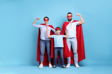 Photo of Parents and their son wearing superhero costumes on light blue background