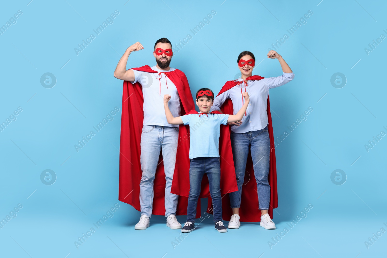 Photo of Parents and their son wearing superhero costumes on light blue background