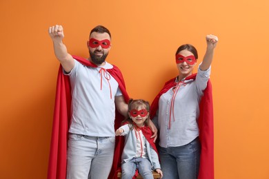 Photo of Parents and their cute little daughter wearing superhero costumes on orange background