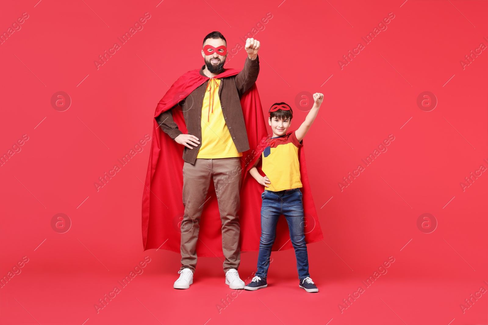 Photo of Father and his son wearing superhero costumes on red background