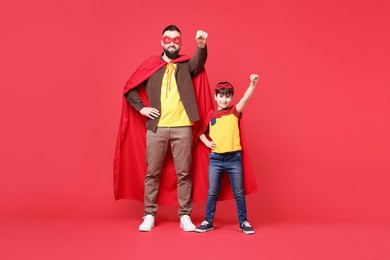 Photo of Father and his son wearing superhero costumes on red background