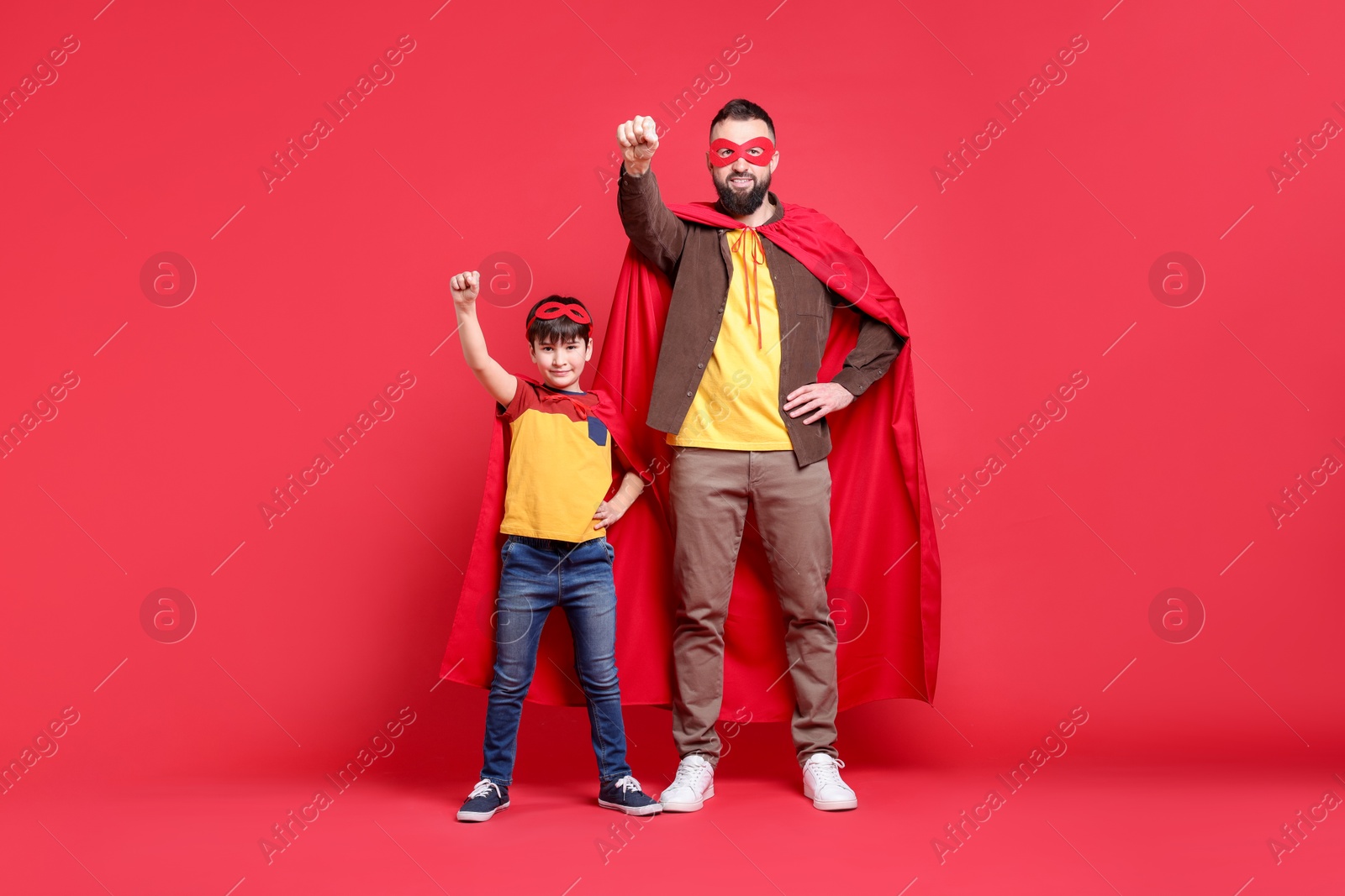 Photo of Father and his son wearing superhero costumes on red background