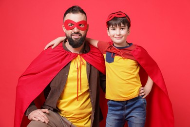 Photo of Father and his son wearing superhero costumes on red background