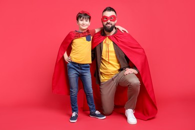 Photo of Father and his son wearing superhero costumes on red background