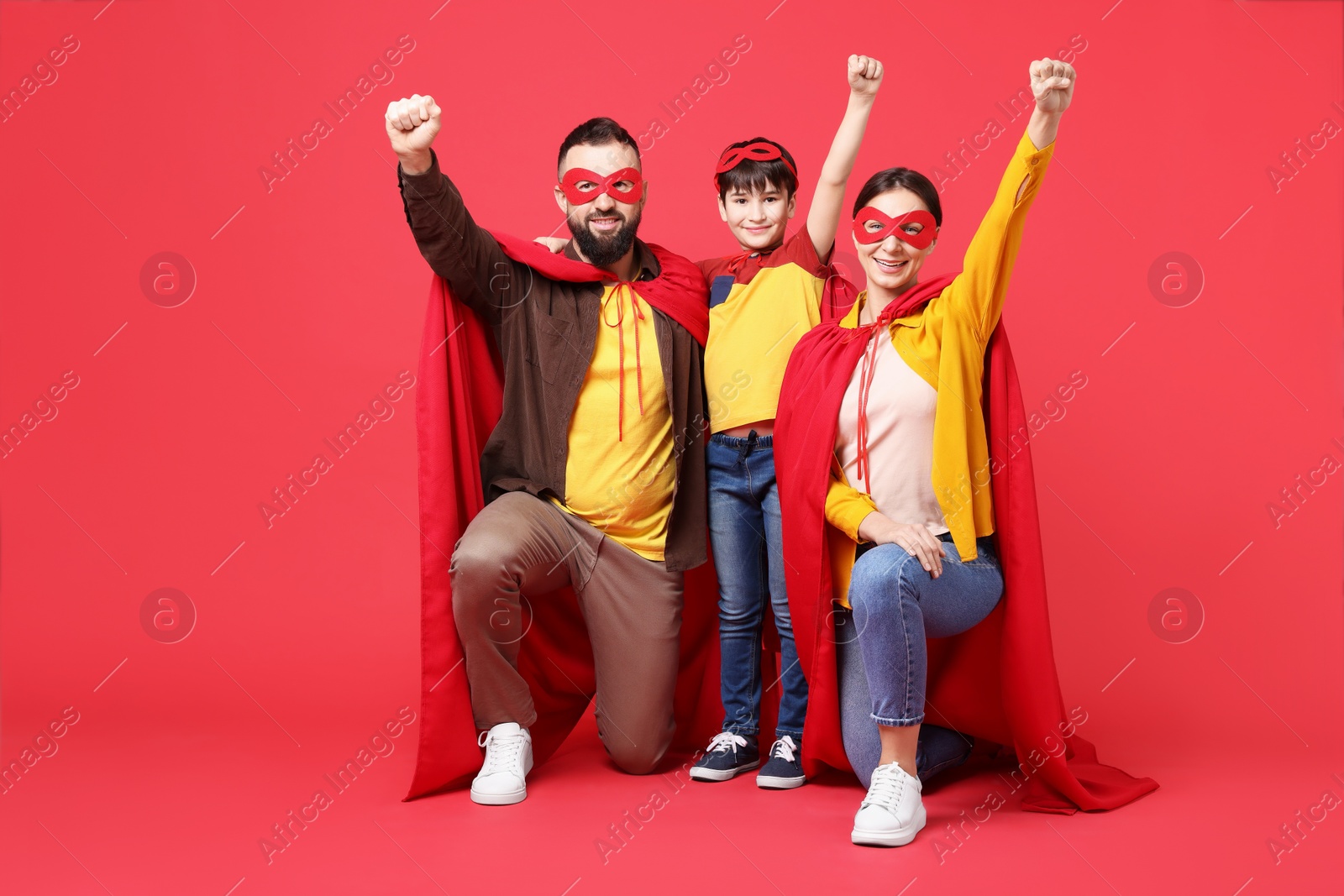 Photo of Parents and their son wearing superhero costumes on red background