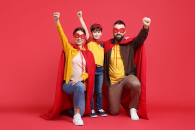 Photo of Parents and their son wearing superhero costumes on red background