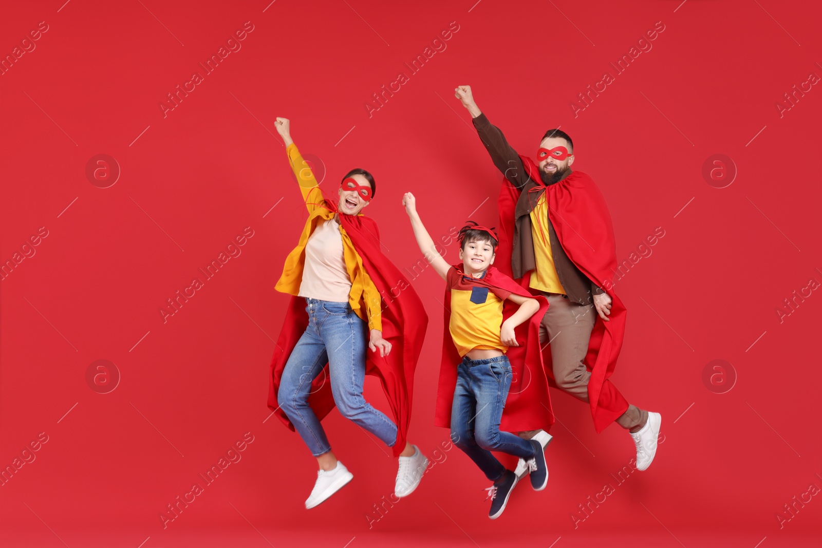 Photo of Parents and their son in superhero costumes jumping on red background