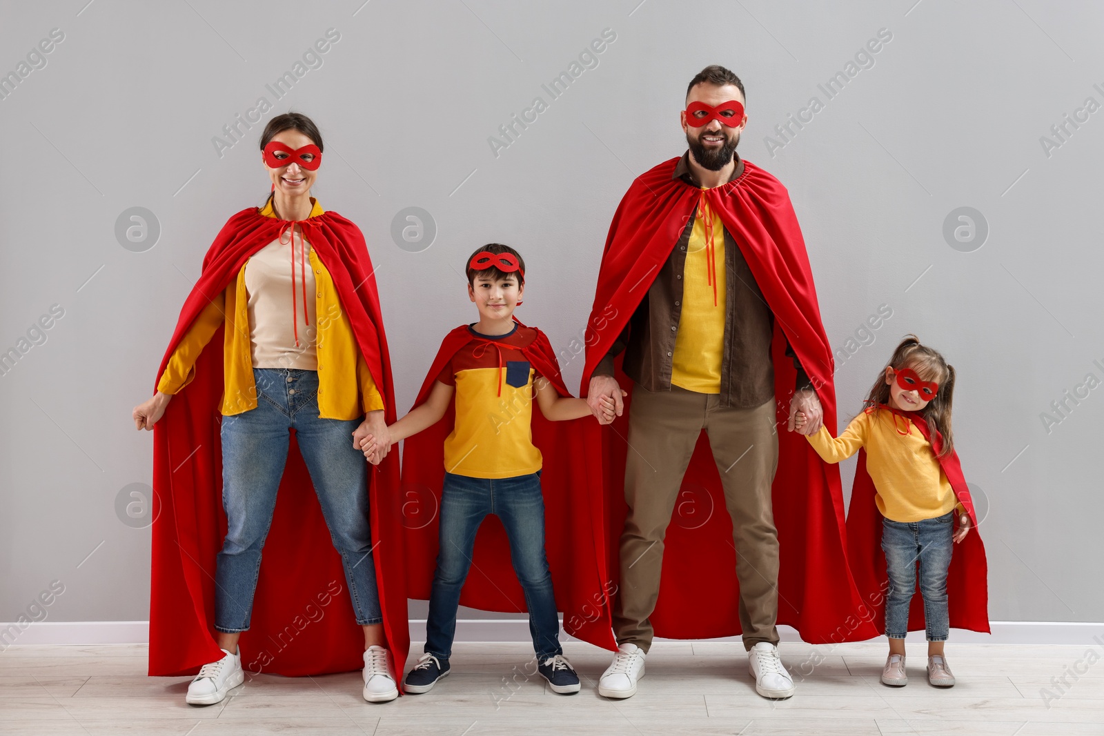 Photo of Parents and their children wearing superhero costumes near light wall indoors