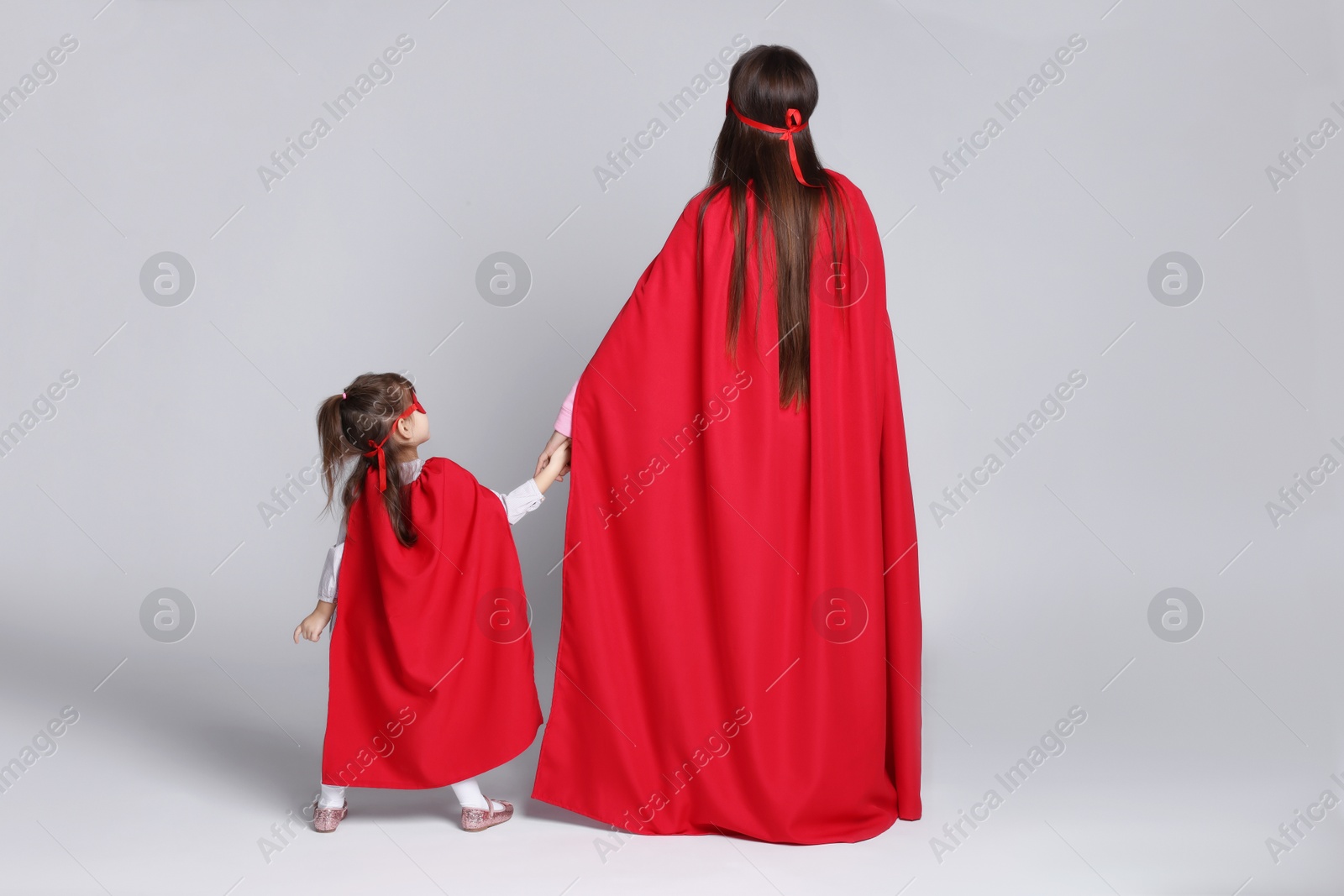 Photo of Mother and her cute little daughter wearing superhero costumes on white background, back view