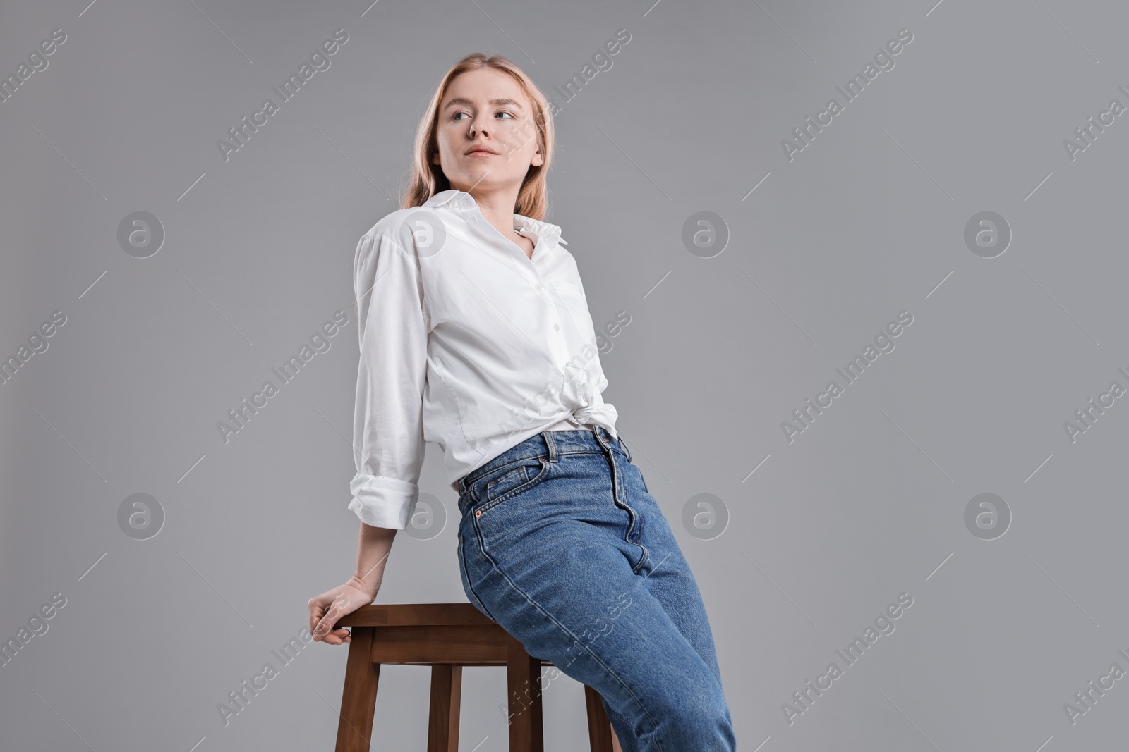 Photo of Woman in stylish jeans sitting on stool against grey background, low angle view