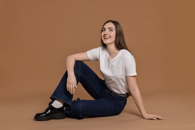 Photo of Smiling woman in stylish jeans on brown background