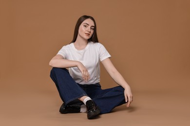 Photo of Beautiful young woman in stylish jeans on brown background