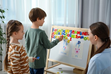 Photo of Speech therapist teaching little kids alphabet with magnetic letters indoors