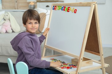 Photo of Little boy learning alphabet with magnetic letters indoors