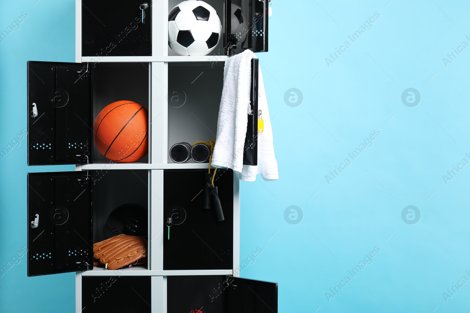 Photo of Open lockers with sport equipment on light blue background, space for text