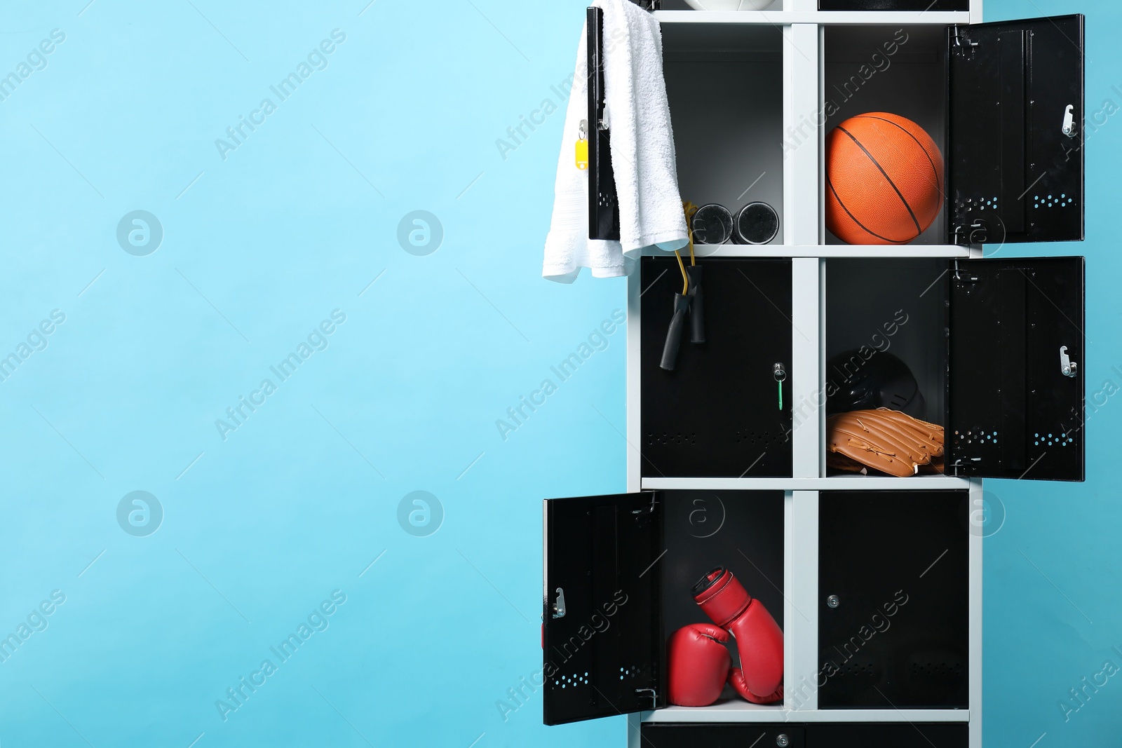 Photo of Open lockers with sport equipment on light blue background, space for text