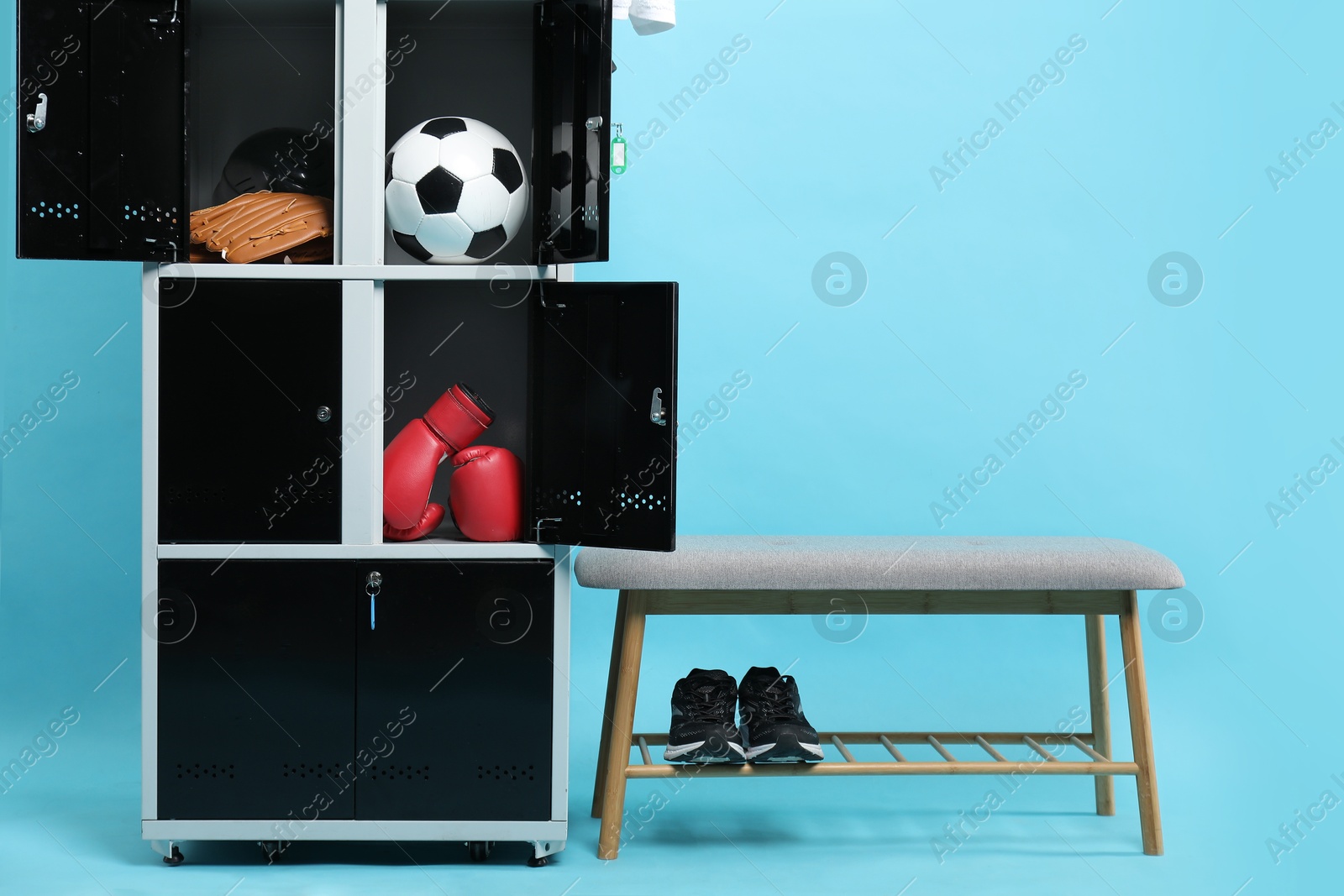 Photo of Open lockers with sport equipment, bench and sneakers on light blue background