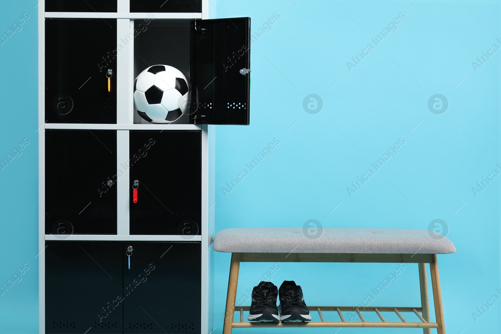 Photo of Open locker with soccer ball, bench and sneakers on light blue background