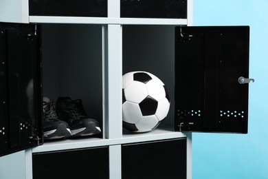 Photo of Open lockers with soccer ball and sneakers on light blue background