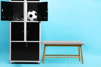 Open lockers with soccer ball, sneakers and bench on light blue background