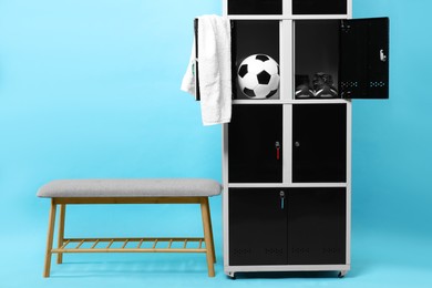 Open lockers with soccer ball, sneakers, towel and bench on light blue background