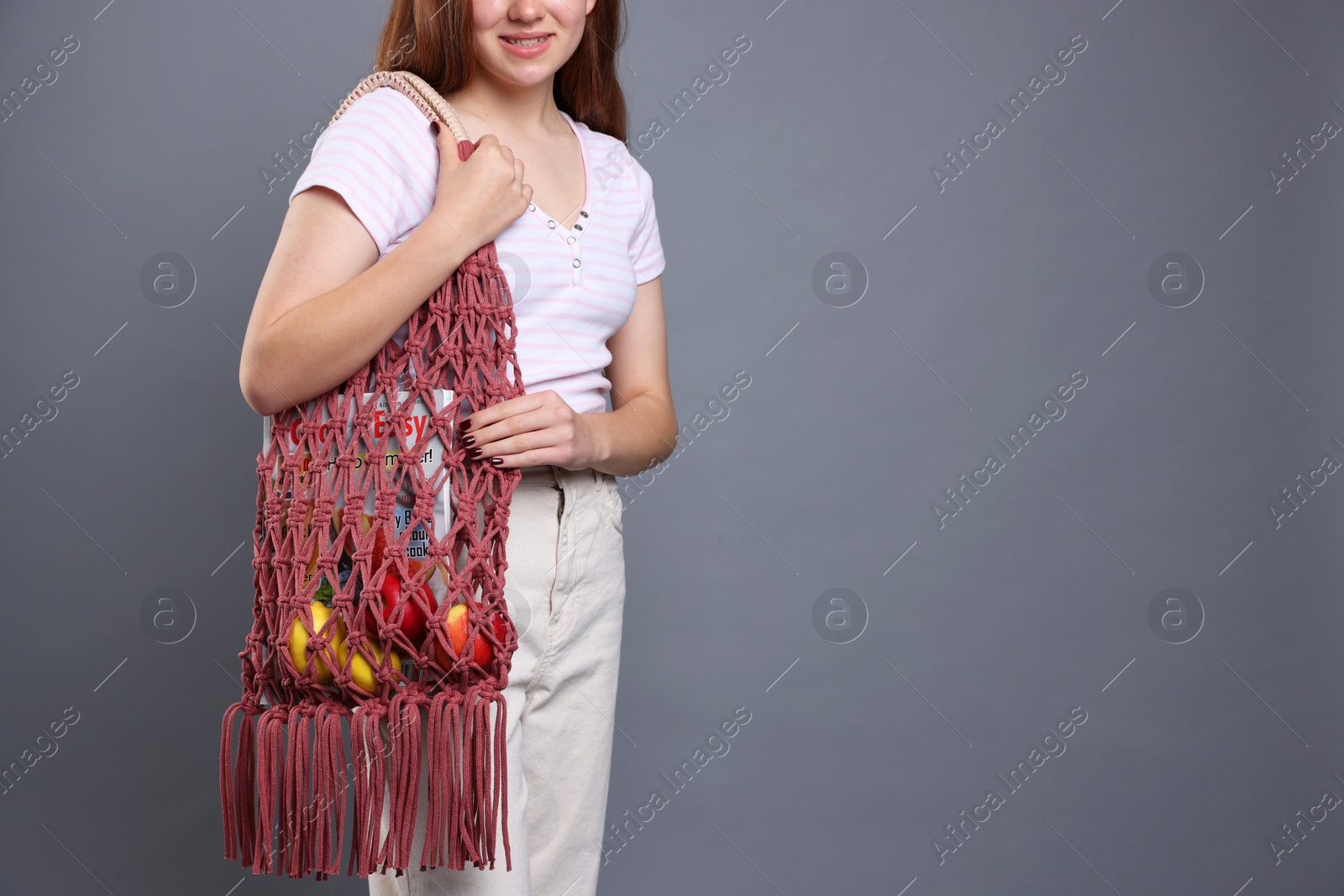 Photo of Teenage girl with handmade macrame bag on grey background, closeup. Space for text