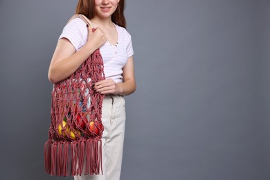 Photo of Teenage girl with handmade macrame bag on grey background, closeup. Space for text