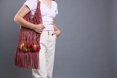 Photo of Teenage girl with handmade macrame bag on grey background, closeup. Space for text