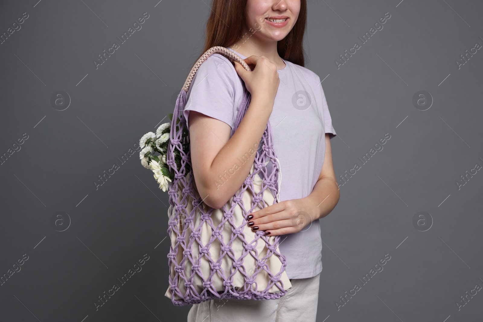 Photo of Teenage girl with handmade macrame bag on grey background, closeup