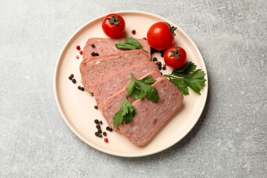 Photo of Pieces of tasty canned meat, parsley, peppercorns and tomatoes on grey textured table, top view