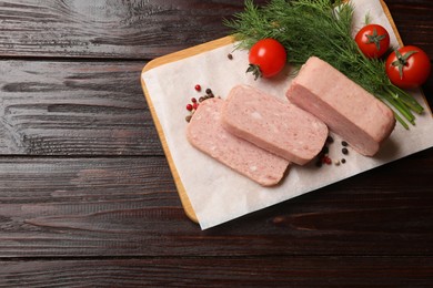 Photo of Pieces of tasty canned meat, tomatoes, dill and peppercorns on wooden table, top view. Space for text