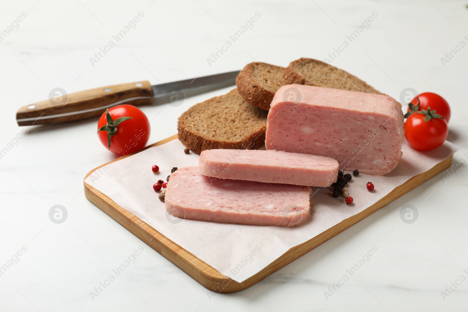 Photo of Pieces of tasty canned meat, tomatoes, peppercorns and bread on white marble table, closeup