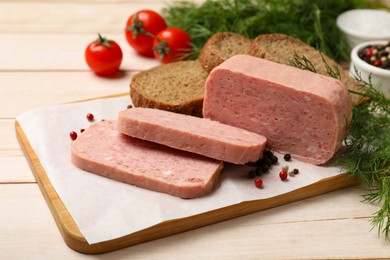 Photo of Pieces of tasty canned meat, peppercorns, dill and bread on light wooden table, closeup