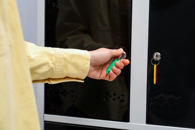 Photo of Woman closing personal locker with key indoors, closeup