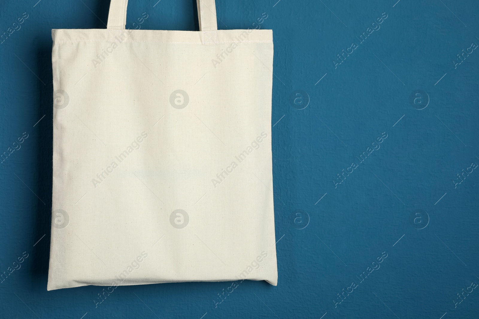 Photo of One eco bag hanging on blue wall. Mockup for design