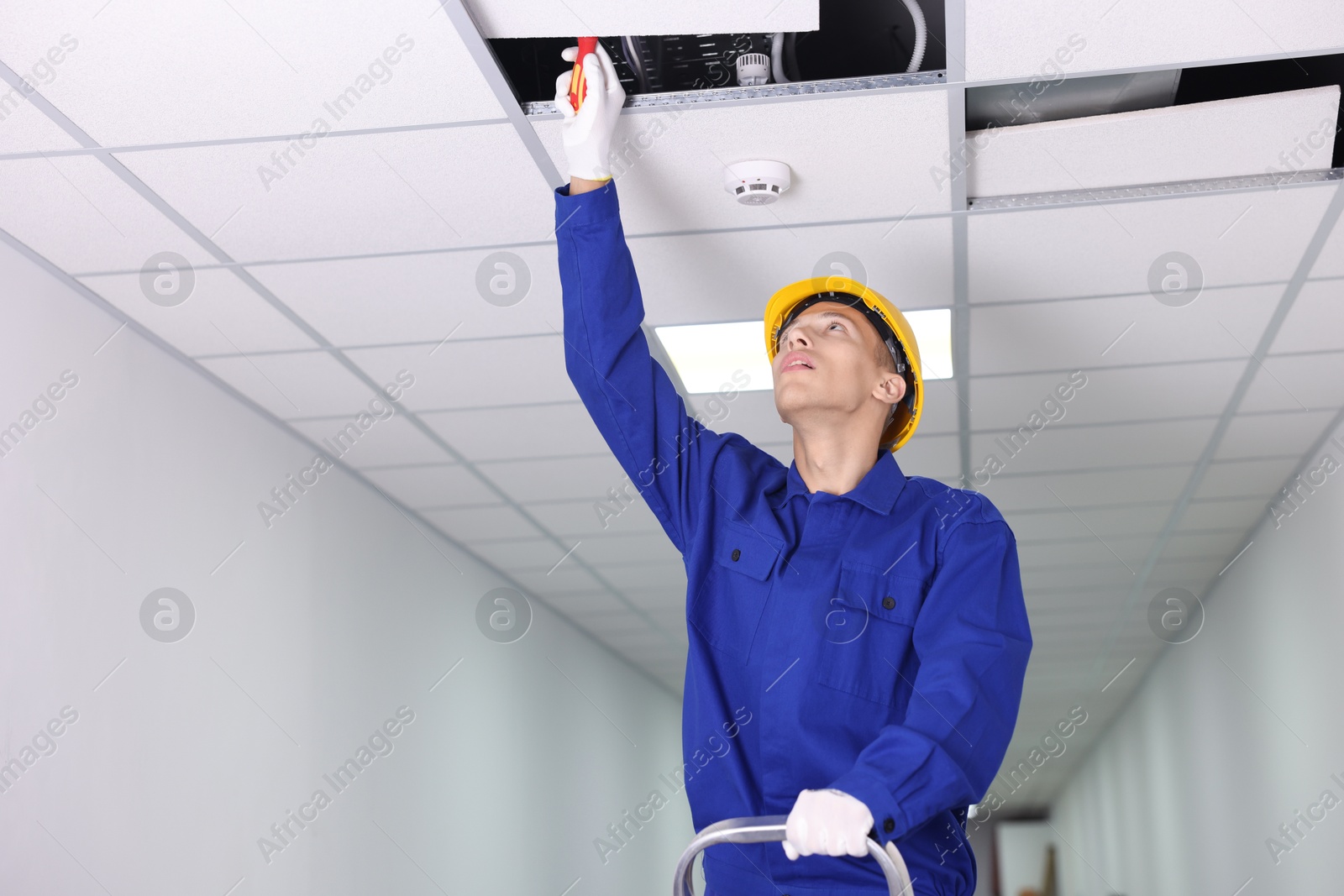 Photo of Suspended ceiling installation. Builder working with PVC tile indoors, low angle view