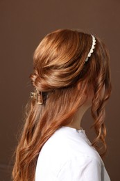 Photo of Teenage girl with stylish hair accessories on brown background, back view