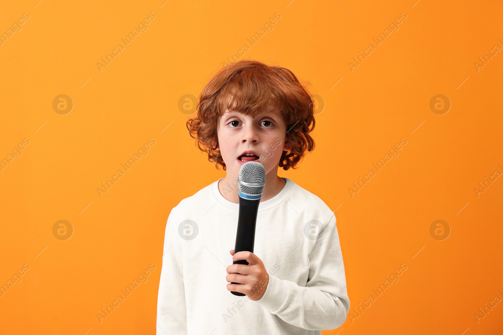 Photo of Little boy with microphone singing on orange background